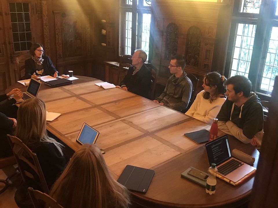 Studierende sammeln sich um einen Tisch und diskutieren einen Vortrag am Studientag Religion, Ritual und Basler Fasnacht 2022